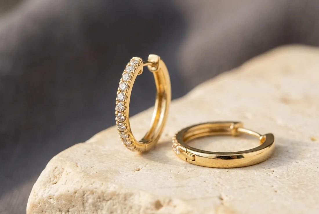 Illustrative yellow gold diamond hoop earrings on ivory stone, with one upright showing the diamond-set front and the other lying flat to reveal the hinge and post.