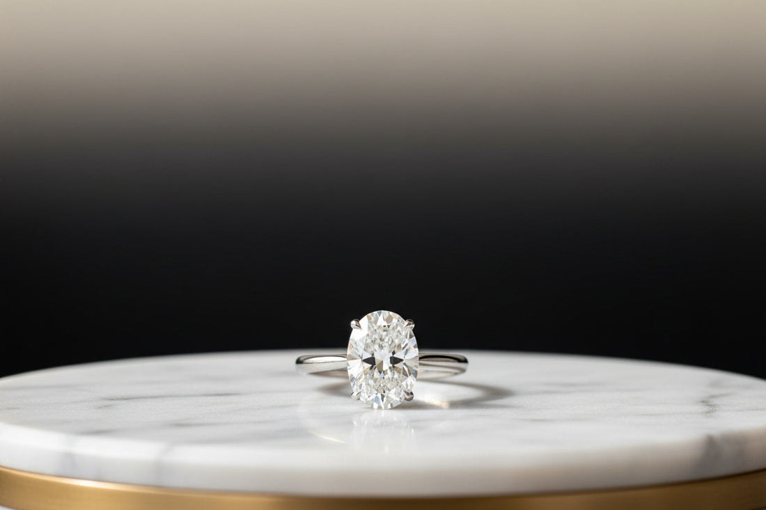 Oval cut diamond solitaire engagement ring in 18K white gold on marble — JewelryRich
