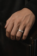Men's 18K white gold hammered wedding band with diamond bezel setting worn on hand, modern groom style