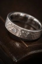 Close-up of hammered brushed texture on 18K white gold men's wedding band with bezel-set diamond center, JewelryRich