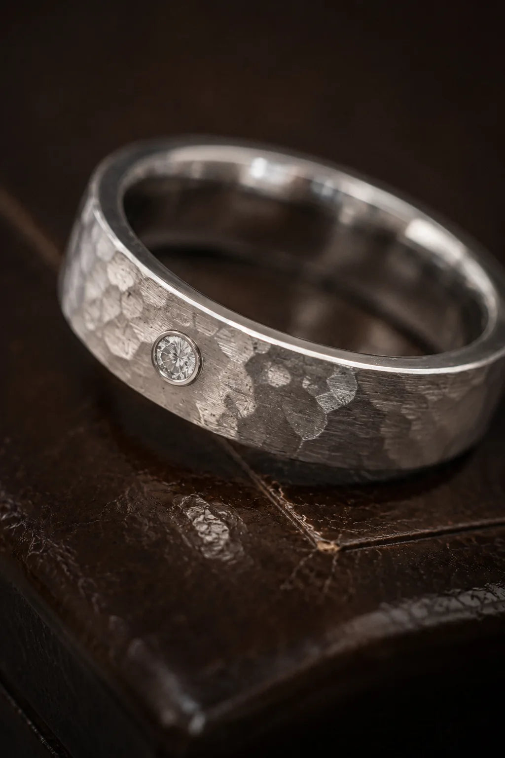 Close-up of hammered brushed texture on 18K white gold men's wedding band with bezel-set diamond center, JewelryRich