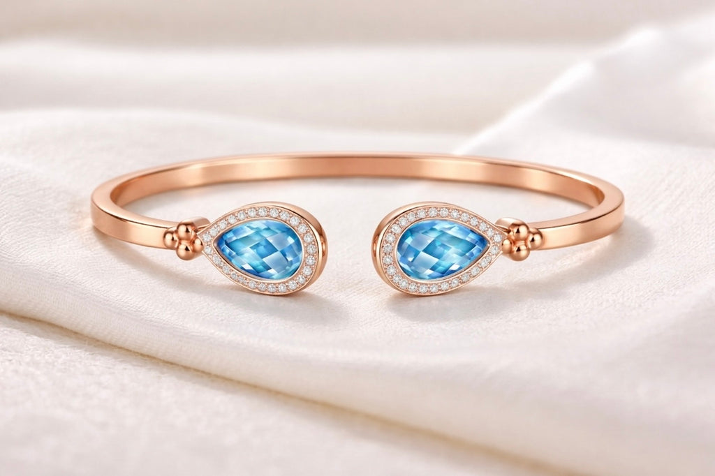 Teardrop Duet Cuff 18K Rose Gold open bangle with Swiss Blue Topaz – flat lay on fabric