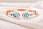 Teardrop Duet Cuff 18K Rose Gold open bangle with Swiss Blue Topaz – flat lay on fabric