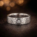 Men's 18K white gold hammered wedding band with single GIA certified diamond bezel setting, product flat lay