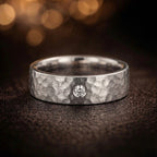 Men's 18K white gold hammered wedding band with single GIA certified diamond bezel setting, product flat lay