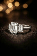 Emerald cut three-stone diamond engagement ring in white gold — angled view on dark background | JewelryRich
