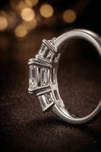 Emerald cut three-stone diamond engagement ring in white gold — side profile view with bokeh background | JewelryRich