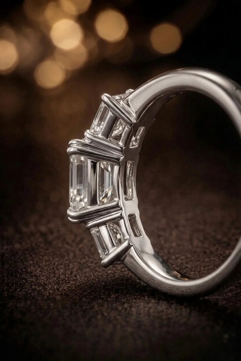 Emerald cut three-stone diamond engagement ring in white gold — side profile view with bokeh background | JewelryRich
